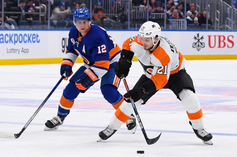 Jan 25, 2022; Elmont, New York, USA; Philadelphia Flyers center Scott Laughton (21) skates the puck across the blue line defended by New York Islanders right wing Josh Bailey (12) during the first period at UBS Arena. Mandatory Credit: Dennis Schneidler-USA TODAY Sports