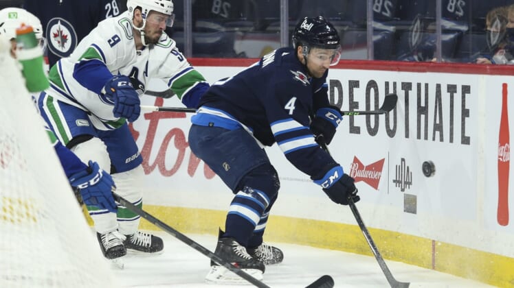 Jan 27, 2022; Winnipeg, Manitoba, CAN;  Winnipeg Jets defenseman Neal Pionk (4) and Vancouver Canucks forward J.T. Miller (9) battle for the put during the first period at Canada Life Centre. Mandatory Credit: Terrence Lee-USA TODAY Sports