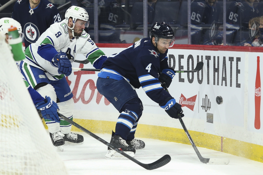 Jan 27, 2022; Winnipeg, Manitoba, CAN;  Winnipeg Jets defenseman Neal Pionk (4) and Vancouver Canucks forward J.T. Miller (9) battle for the put during the first period at Canada Life Centre. Mandatory Credit: Terrence Lee-USA TODAY Sports