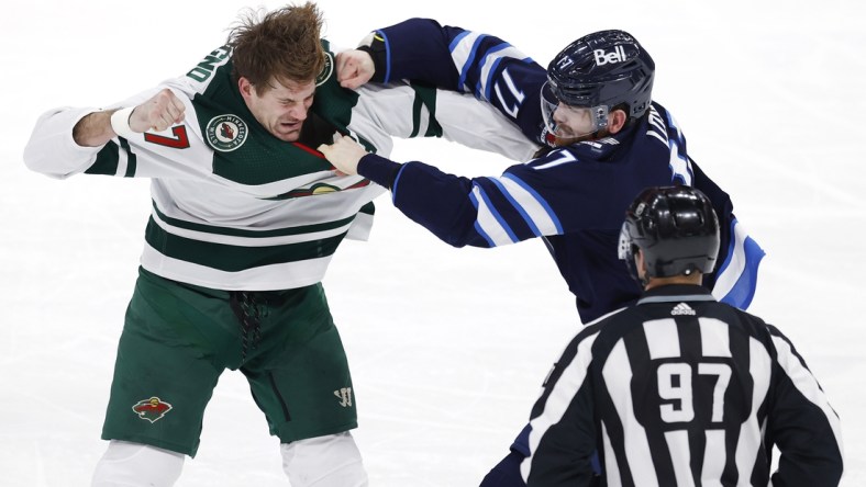 Feb 8, 2022; Winnipeg, Manitoba, CAN; Linesman Kory Nagy (97) watch as Minnesota Wild left wing Marcus Foligno (17) and Winnipeg Jets center Adam Lowry (17) fight in the third period at Canada Life Centre. Mandatory Credit: James Carey Lauder-USA TODAY Sports