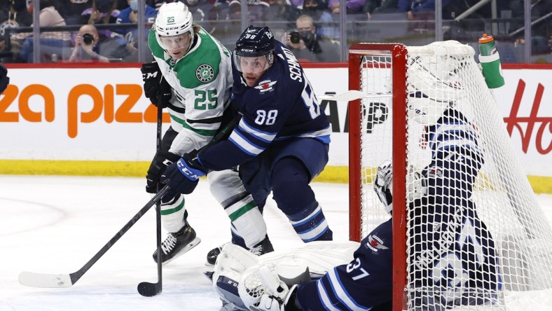 Mar 4, 2022; Winnipeg, Manitoba, CAN; Dallas Stars left wing Joel Kiviranta (25) and Winnipeg Jets defenseman Nate Schmidt (88) dig for the puck under a fallen Winnipeg Jets goaltender Connor Hellebuyck (37) in the first period at Canada Life Centre. Mandatory Credit: James Carey Lauder-USA TODAY Sports