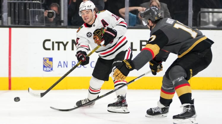 Mar 26, 2022; Las Vegas, Nevada, USA; Chicago Blackhawks left wing Alex DeBrincat (12) shoots in front of Vegas Golden Knights defenseman Ben Hutton (17) during the first period at T-Mobile Arena. Mandatory Credit: Stephen R. Sylvanie-USA TODAY Sports