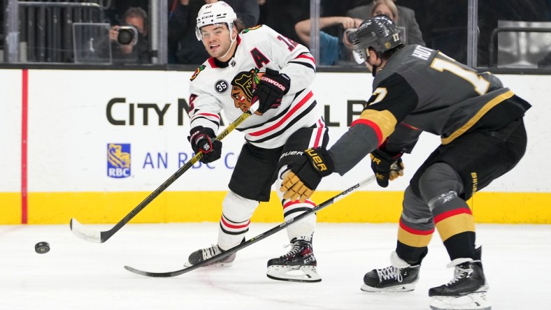 Mar 26, 2022; Las Vegas, Nevada, USA; Chicago Blackhawks left wing Alex DeBrincat (12) shoots in front of Vegas Golden Knights defenseman Ben Hutton (17) during the first period at T-Mobile Arena. Mandatory Credit: Stephen R. Sylvanie-USA TODAY Sports