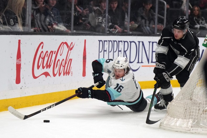 Mar 28, 2022; Los Angeles, California, USA; Seattle Kraken left wing Jared McCann (16) reaches for the puck as LA Kings defenseman Tobias Bjornfot (7) watches in the first period at Crypto.com Arena. Mandatory Credit: Kirby Lee-USA TODAY Sports