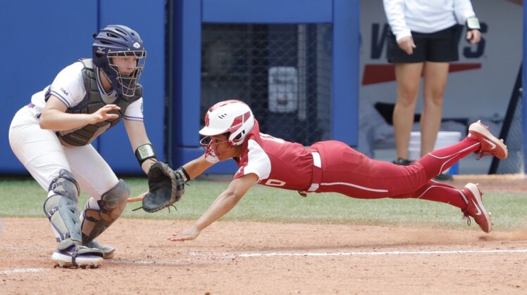 Jun 6, 2021; Oklahoma City, Oklahoma, USA;  Oklahoma s Rylie Boone (0) slides in at home past James Madison catcher Lauren Bernett (22) to score a run in the sixth inning during a Women s College World Series semi finals game at USA Softball Hall of Fame Stadium. Oklahoma won 6-3. Mandatory Credit: Alonzo Adams-USA TODAY Sports