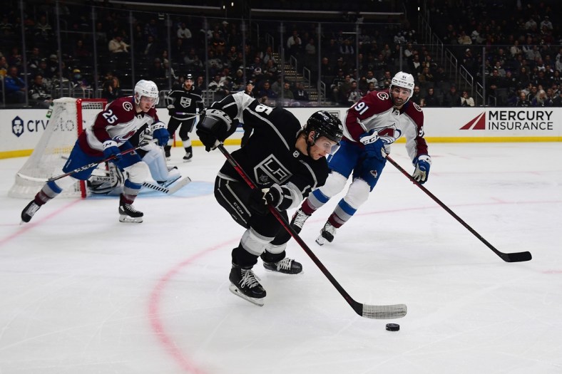 Mar 15, 2022; Los Angeles, California, USA; Los Angeles Kings center Blake Lizotte (46) moves the puck against Colorado Avalanche right wing Logan O'Connor (25) and center Nazem Kadri (91) during the third period at Crypto.com Arena. Mandatory Credit: Gary A. Vasquez-USA TODAY Sports