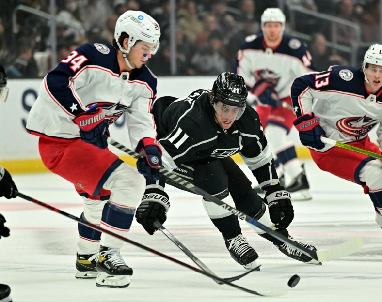Apr 16, 2022; Los Angeles, California, USA;  Los Angeles Kings center Anze Kopitar (11) moves the puck away from Columbus Blue Jackets center Cole Sillinger (34) in the first period of the game at Crypto.com Arena. Mandatory Credit: Jayne Kamin-Oncea-USA TODAY Sports