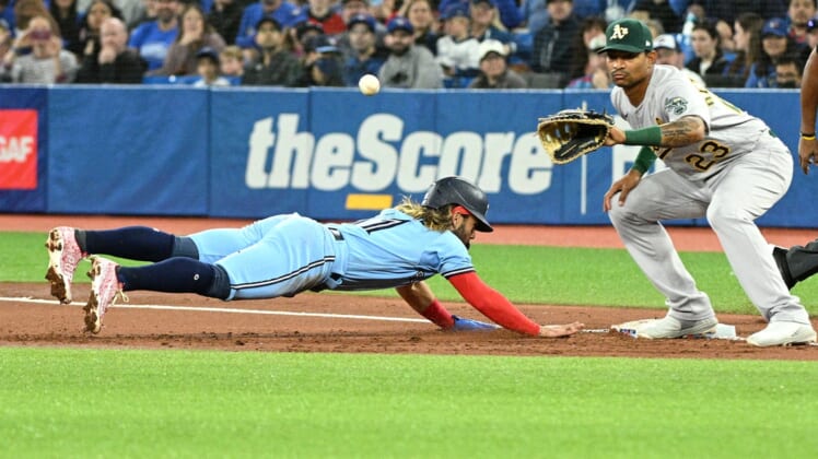Apr 17, 2022; Toronto, Ontario, CAN; Toronto Blue Jays shortstop Bo Bichette (11) dives back to first to avoid a pick off as Oakland Athletics first baseman Christian Bethancourt (23) reaches for the ball in the first inning at Rogers Centre. Mandatory Credit: Dan Hamilton-USA TODAY Sports
