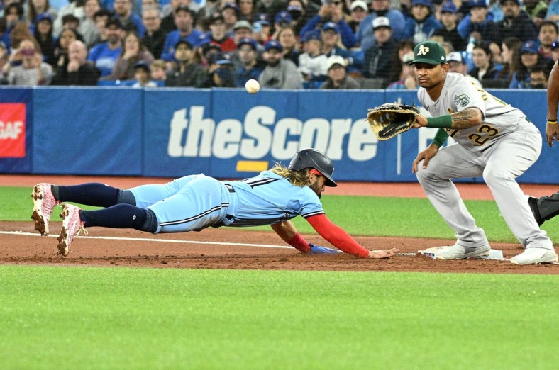 Apr 17, 2022; Toronto, Ontario, CAN; Toronto Blue Jays shortstop Bo Bichette (11) dives back to first to avoid a pick off as Oakland Athletics first baseman Christian Bethancourt (23) reaches for the ball in the first inning at Rogers Centre. Mandatory Credit: Dan Hamilton-USA TODAY Sports