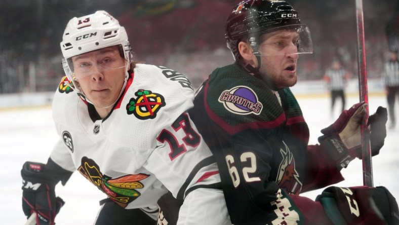 Apr 20, 2022; Glendale, Arizona, USA; Chicago Blackhawks center Henrik Borgstrom (13) and Arizona Coyotes defenseman J.J. Moser (62) battle for position during the first period at Gila River Arena. Mandatory Credit: Joe Camporeale-USA TODAY Sports