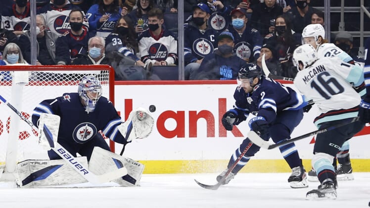 Feb 17, 2022; Winnipeg, Manitoba, CAN; Winnipeg Jets goaltender Eric Comrie (1) makes a glove save on Seattle Kraken left wing Jared McCann (16) in the second period at Canada Life Centre. Mandatory Credit: James Carey Lauder-USA TODAY Sports