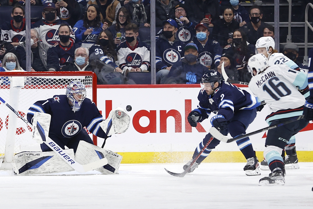 Feb 17, 2022; Winnipeg, Manitoba, CAN; Winnipeg Jets goaltender Eric Comrie (1) makes a glove save on Seattle Kraken left wing Jared McCann (16) in the second period at Canada Life Centre. Mandatory Credit: James Carey Lauder-USA TODAY Sports