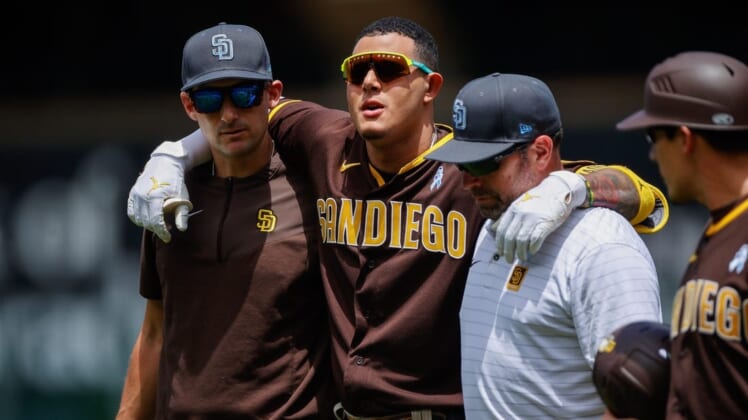 Jun 19, 2022; Denver, Colorado, USA; San Diego Padres third baseman Manny Machado (C) is helped off the field by interim manager Ryan Flaherty (L) and head athletic trainer Mark Rogow (R) after a play at first base in the first inning against the Colorado Rockies at Coors Field. Mandatory Credit: Isaiah J. Downing-USA TODAY Sports