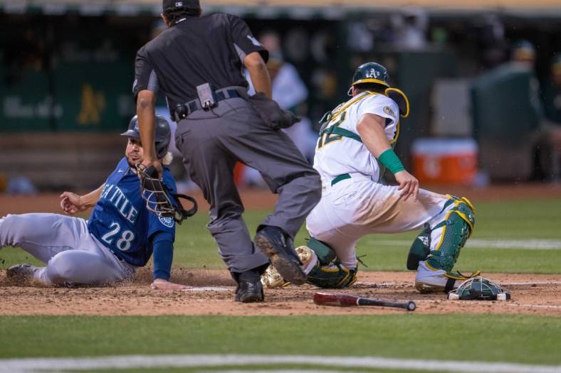 Jun 22, 2022; Oakland, California, USA; Seattle Mariners third baseman Eugenio Suarez (28) slides in safely at home plate during the fifth inning against Oakland Athletics catcher Sean Murphy (12) at RingCentral Coliseum. Mandatory Credit: Neville E. Guard-USA TODAY Sports