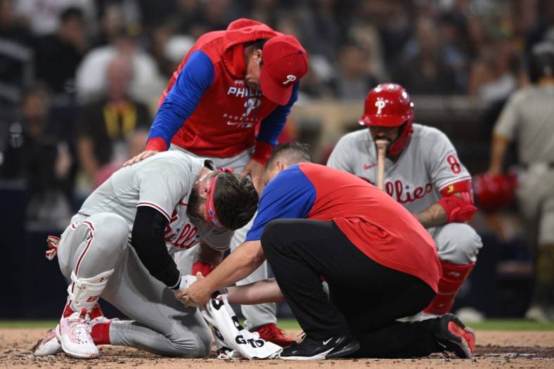 Jun 25, 2022; San Diego, California, USA; Philadelphia Phillies designated hitter Bryce Harper (bottom, left) is checked on by a trainer and interim manager Rob Thomson (top) after being hit by a pitch during the fourth inning against the San Diego Padres at Petco Park. Mandatory Credit: Orlando Ramirez-USA TODAY Sports