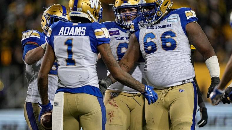 Dec 12, 2021; Hamilton, Ontario, CAN; Winnipeg Blue Bombers offensive lineman Stanley Bryant (66) and offensive lineman Drew Desjarlais (61) congratulate wide receiver Darvin Adams (1) after scoring a touchdown in overtime against the Hamilton Tiger-Cats in the 108th Grey Cup football game at Tim Hortons Field. Mandatory Credit: John E. Sokolowski-USA TODAY Sports