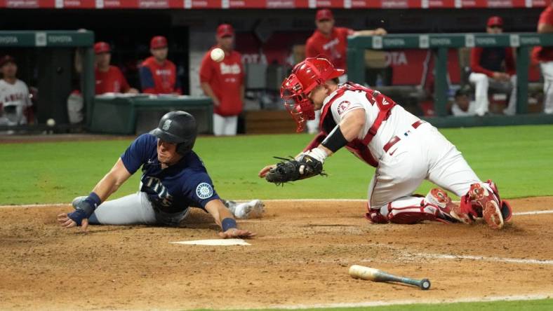 Aug 15, 2022; Anaheim, California, USA; Seattle Mariners right fielder Dylan Moore (25) slides into home plate beating a throw to Los Angeles Angels catcher Max Stassi (33) to score in the ninth inning at Angel Stadium. Mandatory Credit: Kirby Lee-USA TODAY Sports