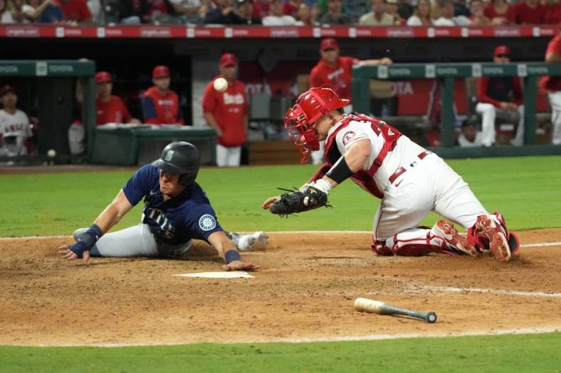 Aug 15, 2022; Anaheim, California, USA; Seattle Mariners right fielder Dylan Moore (25) slides into home plate beating a throw to Los Angeles Angels catcher Max Stassi (33) to score in the ninth inning at Angel Stadium. Mandatory Credit: Kirby Lee-USA TODAY Sports