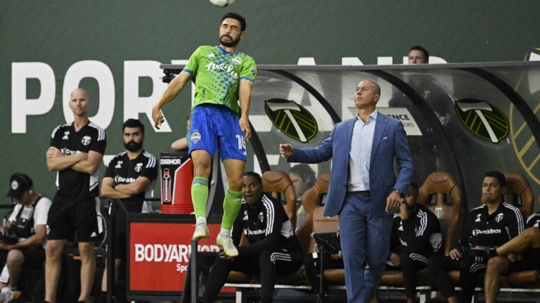 Aug 26, 2022; Portland, Oregon, USA; Seattle Sounders midfielder Alex Roldan (16) heads the ball during the first half next to Portland Timbers head coach Giovanni Savarese at Providence Park. The Timbers won 2-1. Mandatory Credit: Troy Wayrynen-USA TODAY Sports