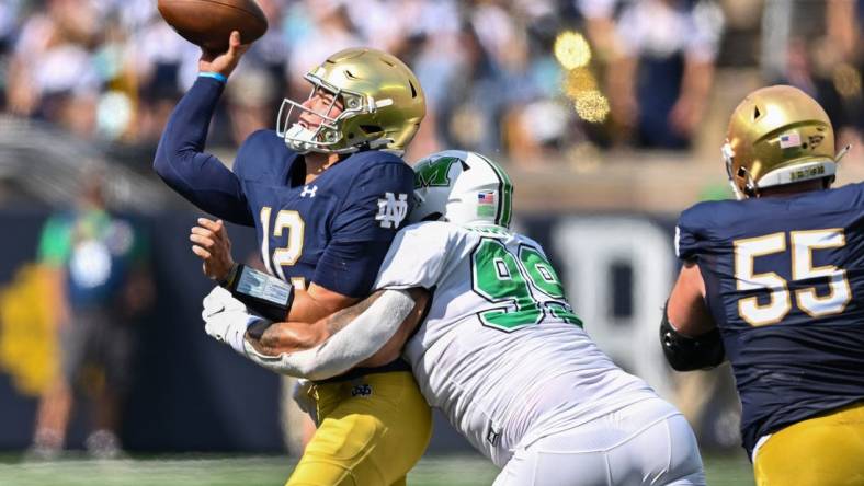 Sep 10, 2022; South Bend, Indiana, USA; Notre Dame Fighting Irish quarterback Tyler Buchner (12) throws as he is hit by Marshall Thundering Herd defensive lineman Isaiah Gibson, Sr. (99) in the first quarter at Notre Dame Stadium. Mandatory Credit: Matt Cashore-USA TODAY Sports