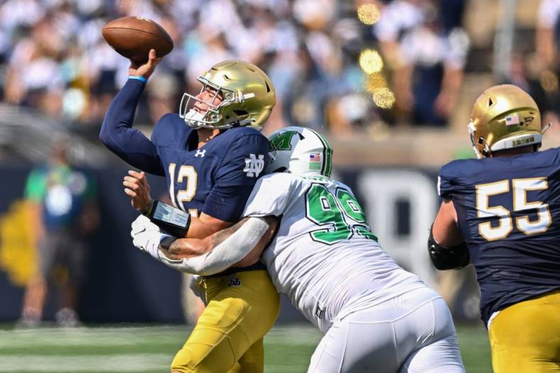 Sep 10, 2022; South Bend, Indiana, USA; Notre Dame Fighting Irish quarterback Tyler Buchner (12) throws as he is hit by Marshall Thundering Herd defensive lineman Isaiah Gibson, Sr. (99) in the first quarter at Notre Dame Stadium. Mandatory Credit: Matt Cashore-USA TODAY Sports