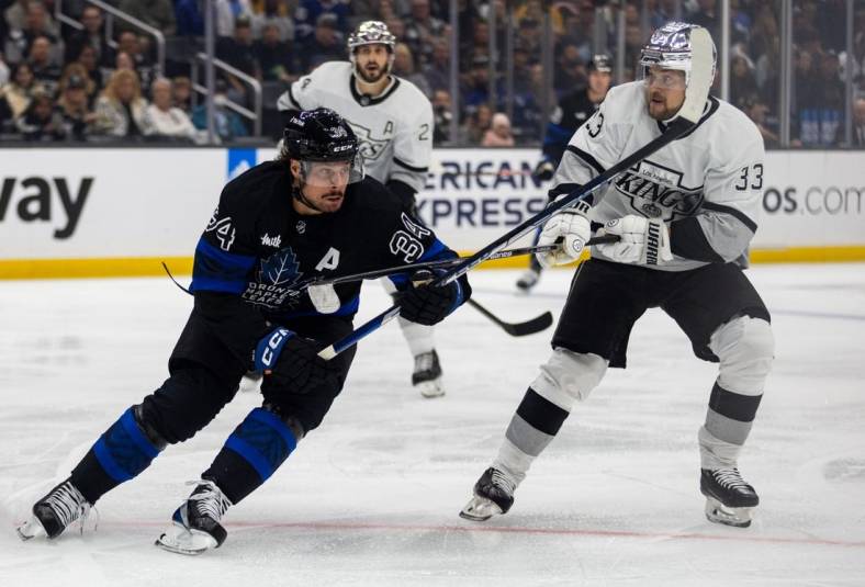 Oct 29, 2022; Los Angeles, California, USA; Toronto Maple Leafs center Auston Matthews (34) and Los Angeles Kings left wing Viktor Arvidsson (33) chase a puck during the 1st period at Crypto.com Arena. Mandatory Credit: Jason Parkhurst-USA TODAY Sports