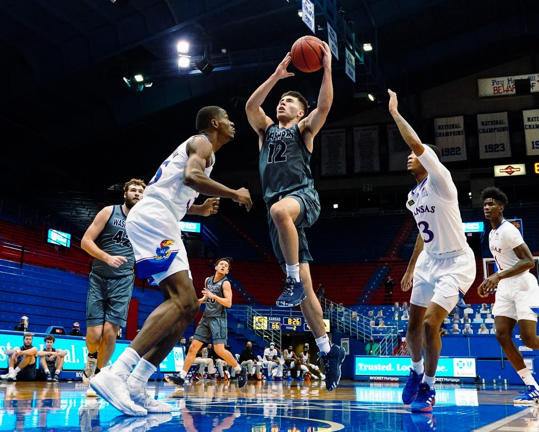 Dec 3, 2020; Lawrence, Kansas, USA; Washburn Ichabods guard Tyler Geiman (12) shoots against Kansas Jayhawks forward Gethro Muscadin (35) and guard Dajuan Harris (3) during the second half at Allen Fieldhouse. Mandatory Credit: Jay Biggerstaff-USA TODAY Sports