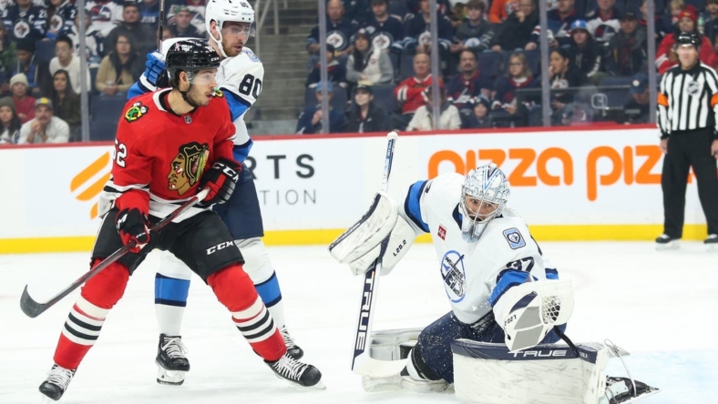 Nov 5, 2022; Winnipeg, Manitoba, CAN; Winnipeg Jets goalie Connor Hellebuyck (37) makes a save as Chicago Blackhawks forward Reese Johnson (52) and Winnipeg Jets forward Pierre-Luc Dubois (80) look for a rebound during the first period at Canada Life Centre. Mandatory Credit: Terrence Lee-USA TODAY Sports