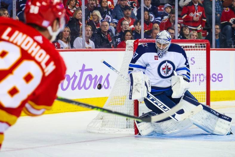 Nov 12, 2022; Calgary, Alberta, CAN; Winnipeg Jets goaltender Connor Hellebuyck (37) makes a save against Calgary Flames center Elias Lindholm (28) during the second period at Scotiabank Saddledome. Mandatory Credit: Sergei Belski-USA TODAY Sports