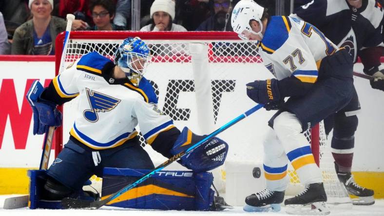 Nov 14, 2022; Denver, Colorado, USA; St. Louis Blues defenseman Niko Mikkola (77) and goaltender Jordan Binnington (50) reach for a loose puck in the third period against the Colorado Avalanche at Ball Arena. Mandatory Credit: Ron Chenoy-USA TODAY Sports