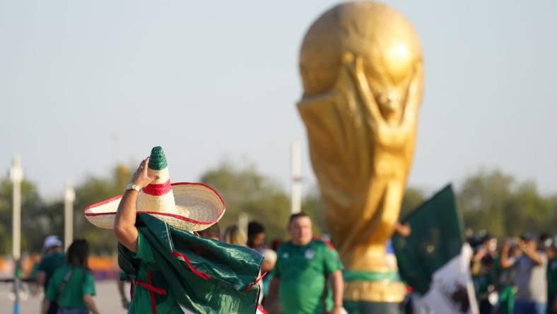 Nov 22, 2022; Doha, Qatar; A Mexico fan wearing a sombrero walks past a World Cup trophy replica outside the stadium before the match against Poland during a group stage match at the 2022 World Cup at Ras Abu Aboud Stadium. Mandatory Credit: Danielle Parhizkaran-USA TODAY Sports