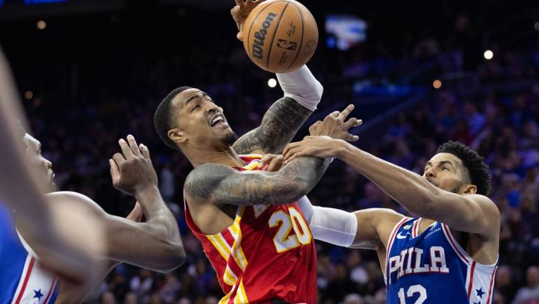 Nov 28, 2022; Philadelphia, Pennsylvania, USA; Atlanta Hawks forward John Collins (20) is fouled while driving for a shot between Philadelphia 76ers forward Tobias Harris (12) and center Joel Embiid (21) during the second quarter at Wells Fargo Center. Mandatory Credit: Bill Streicher-USA TODAY Sports