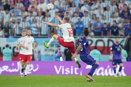 Nov 30, 2022; Doha, Qatar; Poland forward Karol Swiderski (16) leaps for a header past Argentina defender Cristian Romero (13) during the second half in a group stage match during the 2022 World Cup at Stadium 974. Mandatory Credit: Danielle Parhizkaran-USA TODAY Sports
