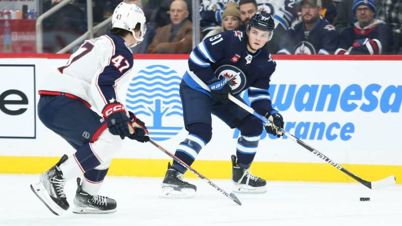 Dec 2, 2022; Winnipeg, Manitoba, CAN;  Winnipeg Jets forward Cole Perfetti (91) looks to pass the puck by Columbus Blue Jackets defenseman Marcus Bjork (47) during the second period at Canada Life Centre. Mandatory Credit: Terrence Lee-USA TODAY Sports