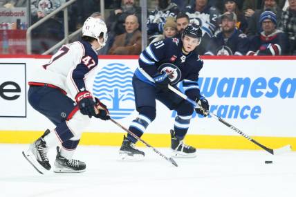 Dec 2, 2022; Winnipeg, Manitoba, CAN;  Winnipeg Jets forward Cole Perfetti (91) looks to pass the puck by Columbus Blue Jackets defenseman Marcus Bjork (47) during the second period at Canada Life Centre. Mandatory Credit: Terrence Lee-USA TODAY Sports