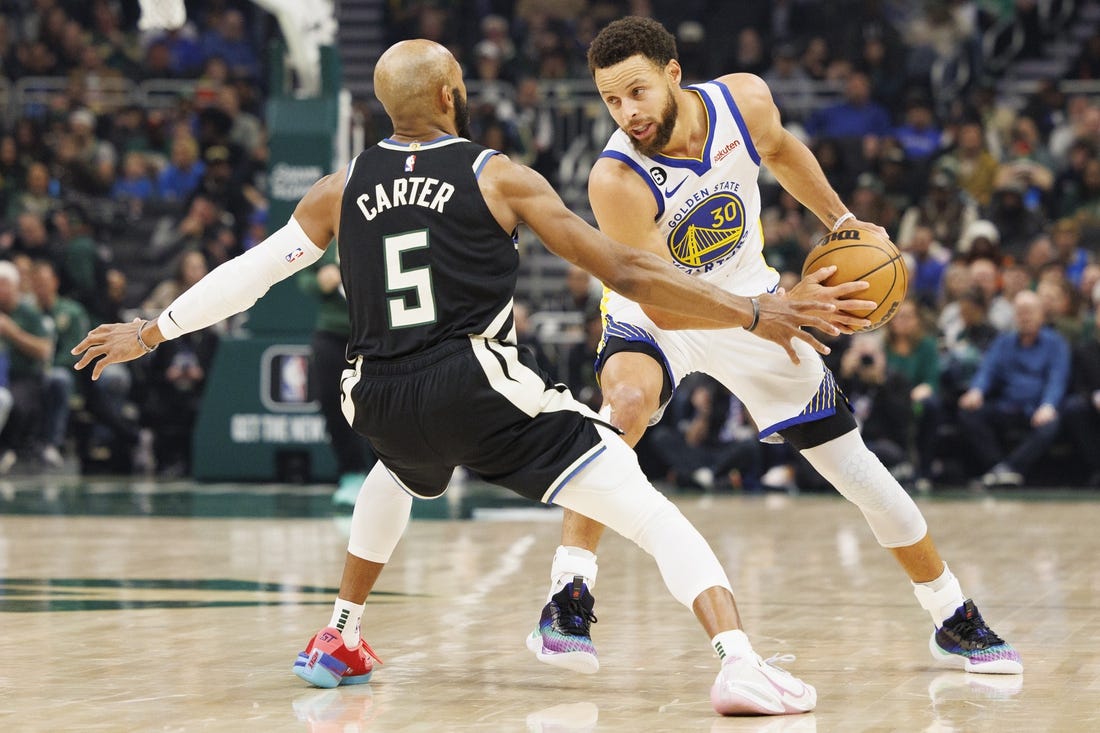 Dec 13, 2022; Milwaukee, Wisconsin, USA;  Golden State Warriors guard Stephen Curry (30) holds the ball away from Milwaukee Bucks guard Jevon Carter (5) during the first quarter at Fiserv Forum. Mandatory Credit: Jeff Hanisch-USA TODAY Sports