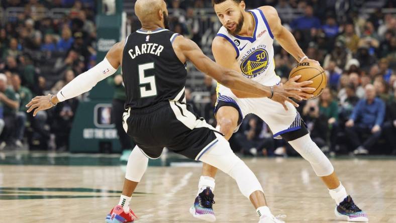 Dec 13, 2022; Milwaukee, Wisconsin, USA;  Golden State Warriors guard Stephen Curry (30) holds the ball away from Milwaukee Bucks guard Jevon Carter (5) during the first quarter at Fiserv Forum. Mandatory Credit: Jeff Hanisch-USA TODAY Sports