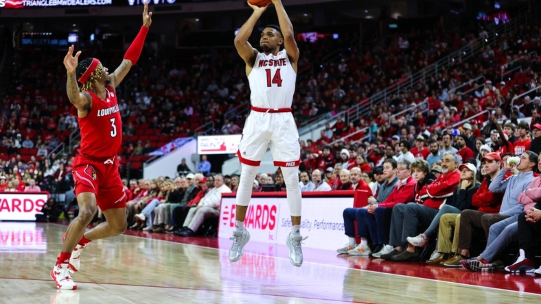Dec 22, 2022; Raleigh, North Carolina, USA;  North Carolina State Wolfpack guard Casey Morsell (14) shoots a three pointer while guard El Ellis (3) tries to block him during the first half against Louisville Cardinals at PNC Arena. Mandatory Credit: Jaylynn Nash-USA TODAY Sports