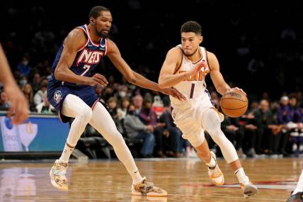Nov 27, 2021; Brooklyn, New York, USA; Phoenix Suns guard Devin Booker (1) drives with the ball around Brooklyn Nets forward Kevin Durant (7) during the first quarter at Barclays Center. Mandatory Credit: Brad Penner-USA TODAY Sports