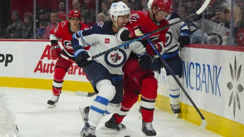 Mar 14, 2023; Raleigh, North Carolina, USA;  Winnipeg Jets defenseman Brenden Dillon (5) checks Carolina Hurricanes center Jesperi Kotkaniemi (82) during the first period at PNC Arena. Mandatory Credit: James Guillory-USA TODAY Sports