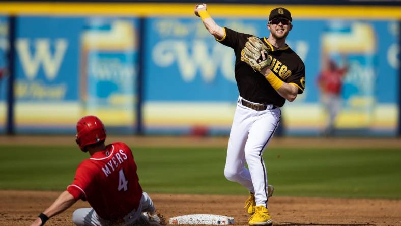 Mar 8, 2023; Peoria, Arizona, USA; San Diego Padres infielder Jake Cronenworth (right) throws to first after coring out sliding Cincinnati Reds base runner Wil Myers during a spring training game at Peoria Sports Complex. Mandatory Credit: Mark J. Rebilas-USA TODAY Sports