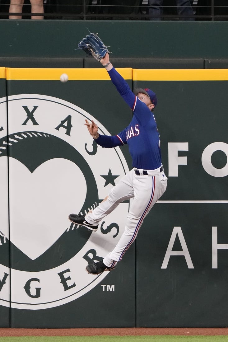 Mar 28, 2023; Arlington, Texas, USA; Texas Rangers left fielder Clint Frazier (77) leaps but is unable to catch the triple hit by Kansas City Royals senior director of hitting performance, major league hitting coach Alec Zumwalt (31) during the eighth inning of an exhibition game at Globe Life Field. Mandatory Credit: Jim Cowsert-USA TODAY Sports