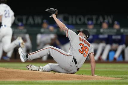 Apr 3, 2023; Arlington, Texas, USA; Baltimore Orioles starting pitcher Kyle Bradish (39) falls to the ground after getting hit by a ball off the bat of Texas Rangers catcher Jonah Heim (28) during the second inning at Globe Life Field. Mandatory Credit: Jim Cowsert-USA TODAY Sports