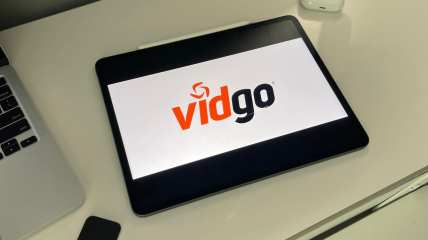 iPad with vidgo logo, remote, and laptop on a desk
