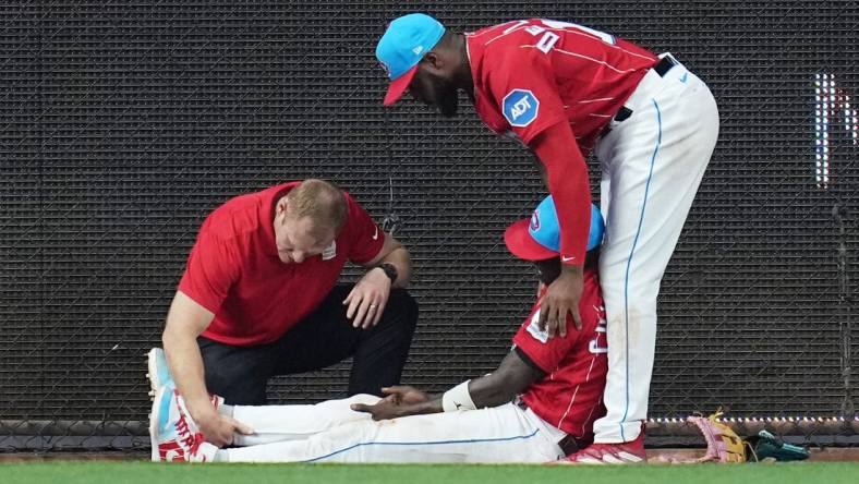 May 13, 2023; Miami, Florida, USA;  Miami Marlins left fielder Bryan De La Cruz (14) holds up center fielder Jazz Chisholm Jr. (2) as he has his leg examined after colliding with the centerfield wall in the eighth inning against the Cincinnati Reds at loanDepot Park. Mandatory Credit: Jim Rassol-USA TODAY Sports