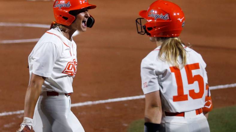 Oklahoma State's Kiley Naomi (5) celebrates a score with Rachel Becker (15) in the first inning during a softball game between Oklahoma State and Utah in the Women's College World Series at USA Softball Hall of Fame Stadium in  in Oklahoma City, Friday, June, 2, 2023.