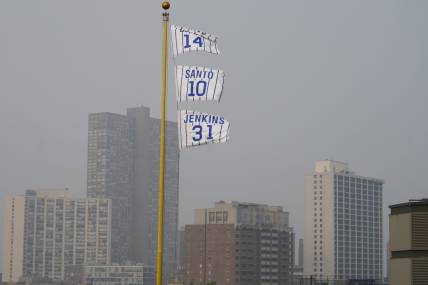 Jun 27, 2023; Chicago, Illinois, USA; The flags of Chicago Cubs' Hall of Fame players Ernie Banks (14), Ron Santo (10) and Ferguson Jenkins fly off the Wrigley Field left field foul pole as a veil of haze from Canadian wildfires shroud high rise buildings along Lake Michigan before a baseball game between the Cubs and the Philadelphia Phillies at Wrigley Field. Mandatory Credit: David Banks-USA TODAY Sports