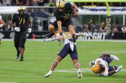 Aug 31, 2023; Orlando, Florida, USA; UCF Knights quarterback John Rhys Plumlee (10) jumps over Kent State Golden Flashes safety Bryce Sheppert (27) during the first quarter at FBC Mortgage Stadium. Mandatory Credit: Mike Watters-USA TODAY Sports battle for the ball