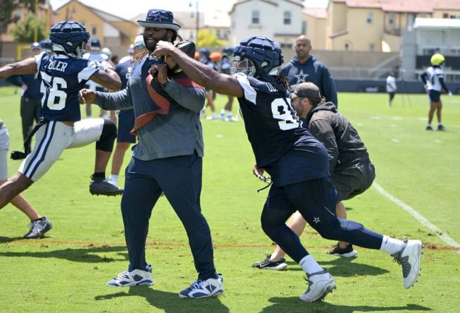 Jul 26, 2023; Oxnard, CA, USA;  Dallas Cowboys defensive end DeMarcus Lawrence (90) reaches around assistant defensive line coach Sharrif Floyd during training camp drills at River Ridge Playing Fields in Oxnard, CA. Mandatory Credit: Jayne Kamin-Oncea-USA TODAY Sports
