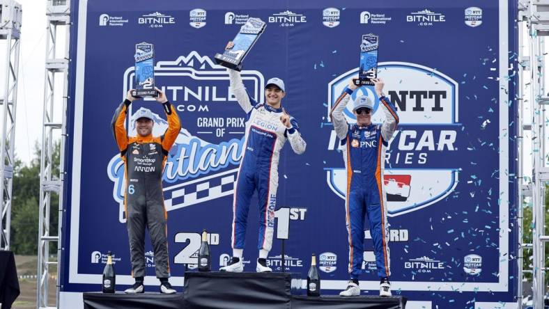 Sep 3, 2023; Portland, Oregon, USA; NTT Indy Car driver Alex Palou (center) lifts his first place trophy with second place finisher Felix Rosenqvist (left) and third place finisher Scott Dixon (right) at Portland International Raceway. Mandatory Credit: Soobum Im-USA TODAY Sports